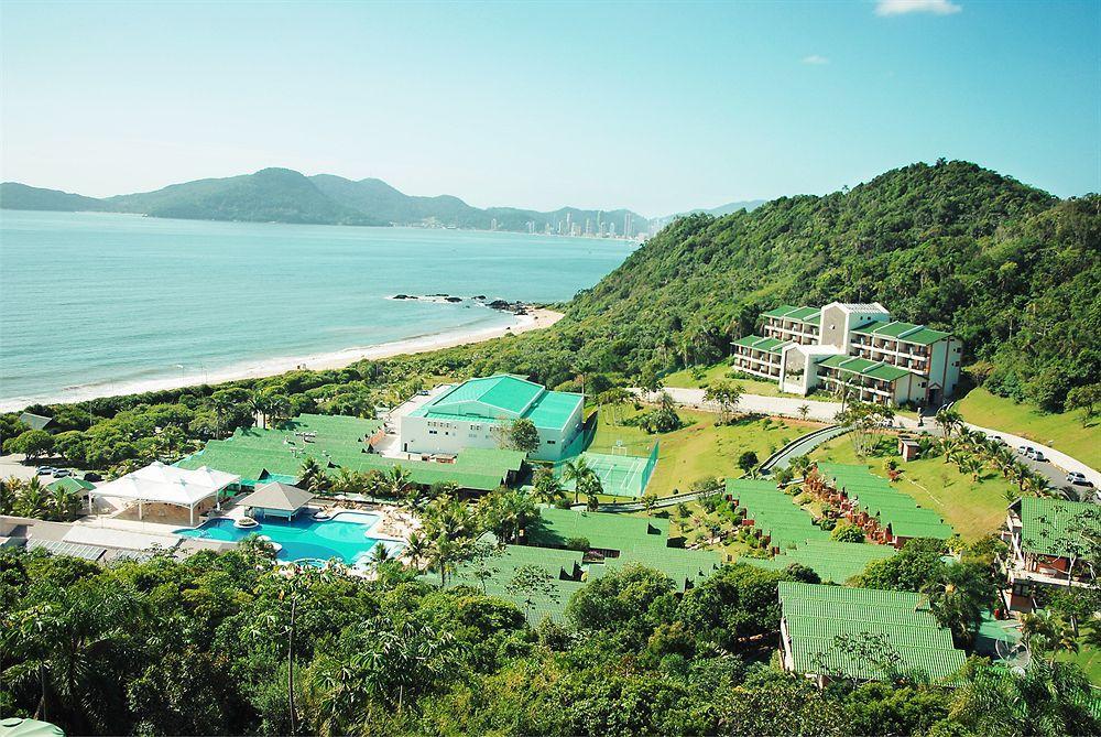 Vista do resort Infinity Blue com piscina, prédios, muito verde e a praia ao fundo.